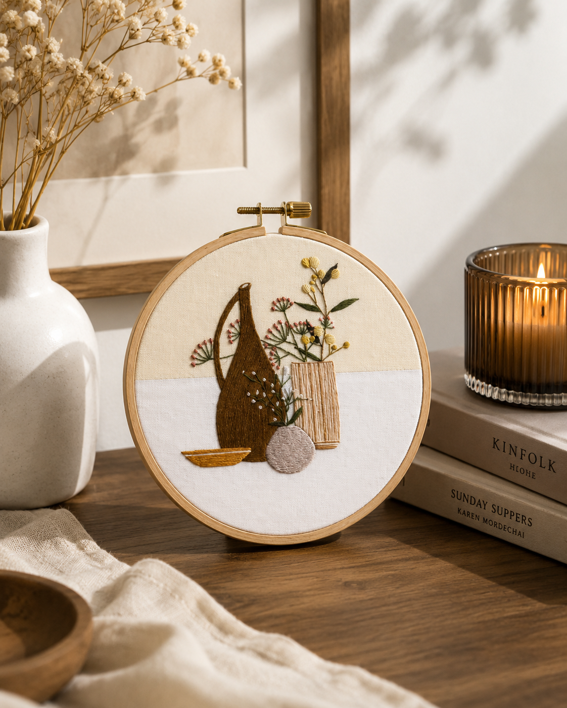 Embroidery hoop with floral design on a wooden surface with books and a candle.