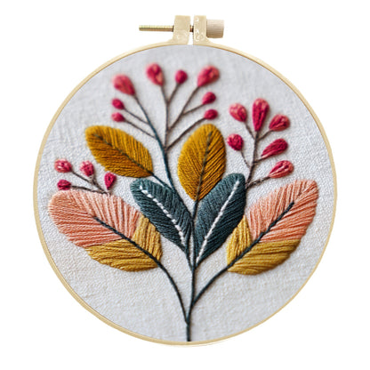 A circular embroidery hoop containing a floral design with embroidered leaves and berries on white fabric, photographed against a plain white background.